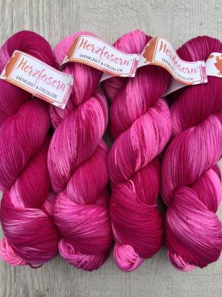 1.	Vier Stränge pink handgefärbte Wolle Herzfasern No. 27 „Pink Inferno“, nebeneinandergelegt auf hellem Holzhintergrund. 	2.	Detailaufnahme eines Strangs Herzfasern No. 27 „Pink Inferno“ mit kräftigen Pink- und Beerentönen. 	3.	Mehrere Stränge Herzfasern